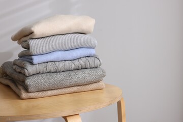 Stack of woolen sweaters on wooden table against light background. Space for text