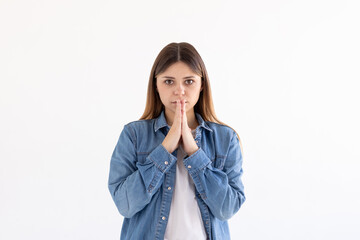 Portrait of imploring girl tilts head, purses lips, looks sadly at camera, makes praying gesture,...