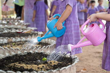 Children in purple uniforms water garden beds with colorful watering cans, nurturing young plants....