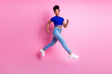 Happy young woman in casual fashion performs a joyous jump against a vibrant pink background...