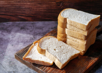 A stack of  white bread slices against Bread Sliced on Wooden Cutting Board