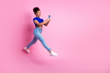 Excited young woman holding a smartphone while jumping against a pink background showcasing vibrant...