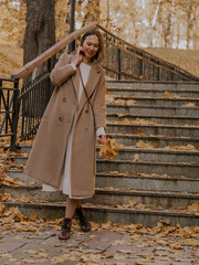 Beautiful blonde young woman in hat and coat walking on the stairs in the autumn park.