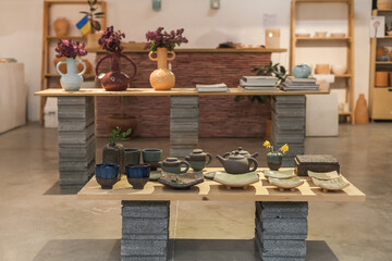 Artisanal ceramic home decor in a minimalist showroom. Handcrafted vases, candle holders, and tableware in earth tones. Includes Easter-themed ceramics and in-store workshop scenes