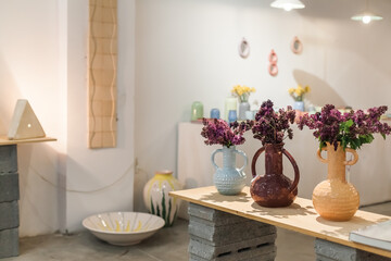 Artisanal ceramic home decor in a minimalist showroom. Handcrafted vases, candle holders, and tableware in earth tones. Includes Easter-themed ceramics and in-store workshop scenes