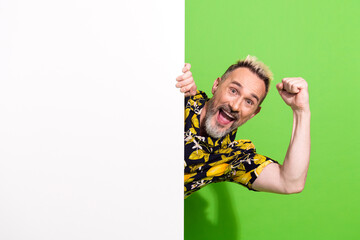 Excited middle aged man with blond dyed hair gesturing enthusiastically against a green background,...