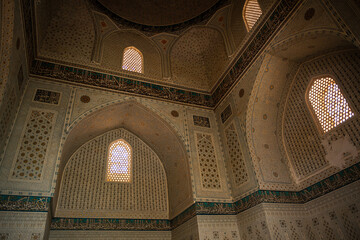 Naklejka premium Interior of Gur e Amir mausoleum in Samarkand with intricate Islamic patterns, gold details, arabesque mosaic, decorative arches, calligraphy illuminated by sunlight through lattice windows