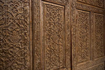 Traditional Islamic wooden door with intricate carved floral and geometric patterns close up, antique handcrafted design detail in historic architecture of Central Asia, cultural heritage texture