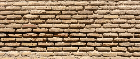 Close-up view of traditional handmade clay brick wall texture in bright, showing historic architecture details with irregular shapes, rustic surface and aged mortar joints in ancient construction