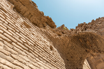 Ancient clay brick arch and wall in ruins under bright sky, close-up low angle view of historical architecture with textured masonry, eroded edges and sunlight on traditional handmade construction