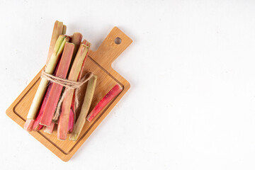 Raw fresh organic rhubarb stems on kitchen table background, bunch of homegrown pink and green rhubarb ready for cooking, on cutting board. Summer harvest, summer food and dessert cooking ingredient