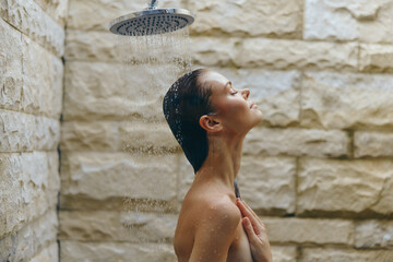 woman relaxing in outdoor shower under rainfall, peaceful moment with natural stone wall background, enjoying refreshing water cascade on skin