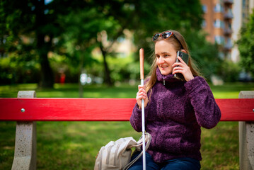 A visually impaired woman with white cane sitting in the city park