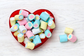 Colorful marshmallows in a heart-shaped plate on a white wooden table