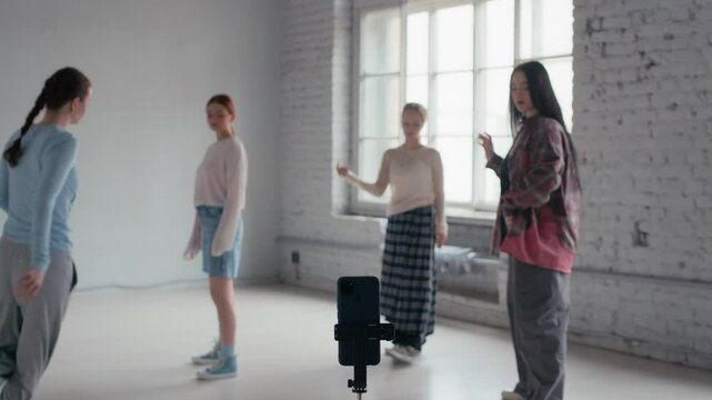 Long shot of four female Caucasian zoomers filming their dance on smartphone in tripod in modern minimalist studio