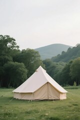 A large beige bell - shaped tent set up in a lush green meadow with rolling hills in the background under a cloudy sky