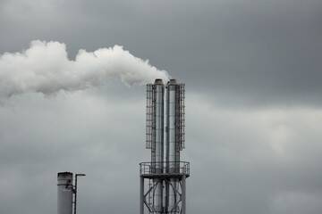 Industrial factory smokestacks emitting white smoke against gloomy cloudy sky, air pollution and environmental damage concept