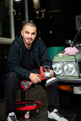 A young man polishing an old-timer car in his garage