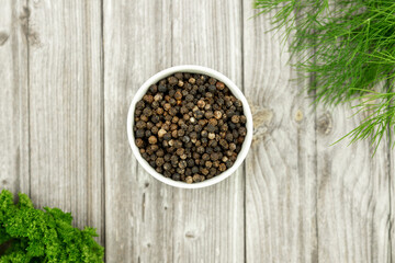 Black peppercorns in a white plate. A hot spice for cooking. Pepper, parsley, dill. 