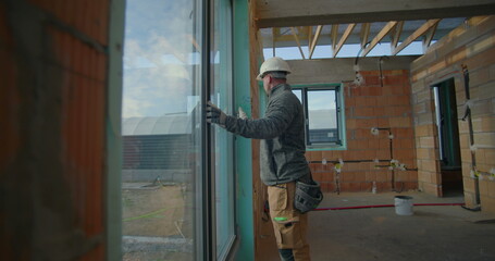 Fototapeta premium Worker inspecting window installation during residential construction project, wearing hard hat, ensuring alignment and quality standards on site