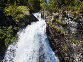 Powerful forest waterfall in Norway: a refreshing cascade among rocks and bright greenery in the...