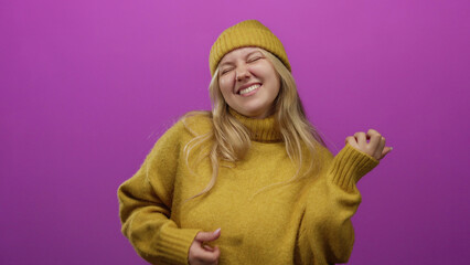 Young blonde woman wearing mustard sweater mimicking guitar on pink background, expressing joy.