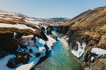 Early spring view of Studlagil Canyon with melting snow and basalt walls...