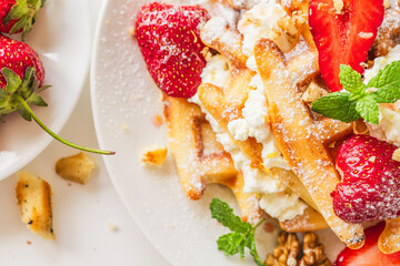Belgian waffles with cottage cheese cream, strawberries, walnuts and mint on a white plate on a light table with a cup of coffee. Delicious, Sunday breakfast.