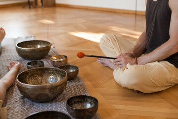 Sound healing ceremony in a yoga studio with Tibetan singing bowls, incense, and meditating participants. Peaceful atmosphere with natural light and warm tones