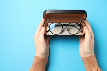 Woman with glasses in case on light blue background, top view
