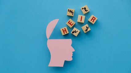 Heir text on wooden cubes and pink paper figure of a human head on blue background