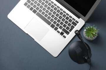 Professional microphone, laptop and floral decor on grey background, flat lay