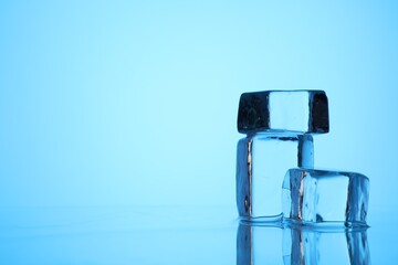 Cubes of clear ice on light blue background, closeup. Space for text