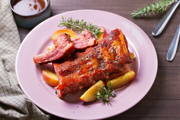 Roasted rack of pork ribs with apples on a plate and brown wood background