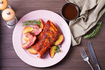 Roasted rack of pork ribs with apples on a plate and brown wood background. High angle view
