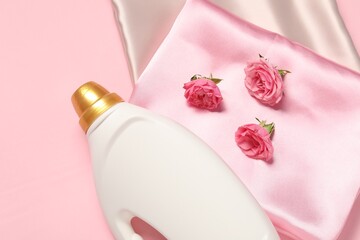 Bottle of fabric softener, flowers and color fabrics on pink background, flat lay