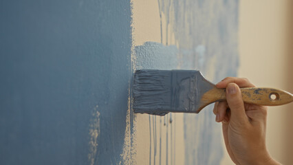 Woman painting wall with blue color brush in a new home interior, showcasing hand holding tool in modern apartment setting for creative decoration.