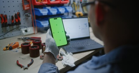 Man Checking Real-Time Stocks, Exchange Market Charts on Laptop and Smartphone with Green Screen Mock Up in Workshop. Video Template with Placeholder for Application or Business Advertising. Close Up.