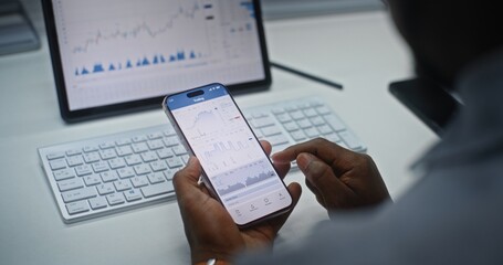 African American Stock Exchange Trader Analyzing Real-Time Stocks and Exchange Market Charts on Smartphone and Tablet Computer Using Online Trading App. Investment Agent Working in Office. Close Up.