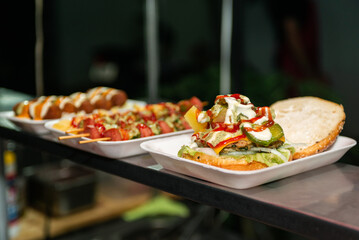 Close-up of a freshly prepared burger, garnished with various toppings, resting on a disposable white tray