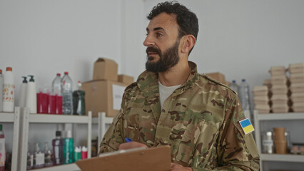 Hispanic bearded man in military uniform standing indoors with clipboard, surrounded by supplies...