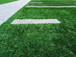 Bright green turf American football or soccer field surface with white sidelines and yard line markings. Overhead view. - obrazy, fototapety, plakaty