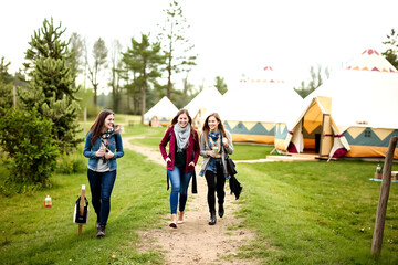 Three friends strolling towards a vibrant festival campsite on a sunny day