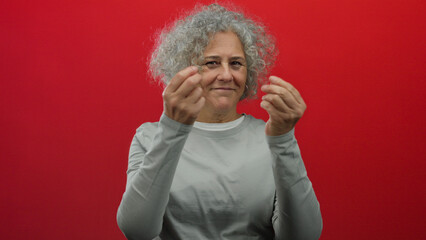Woman with grey hair gesturing on a vivid red background, expressive and confident, capturing elegance and maturity in a simple pose, isolated from distractions.