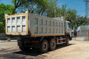 Dump truck positioned on construction zone delivering asphalt for resurfacing, fencing, utility poles, and construction barriers, highlighting active urban infrastructure improvement project
