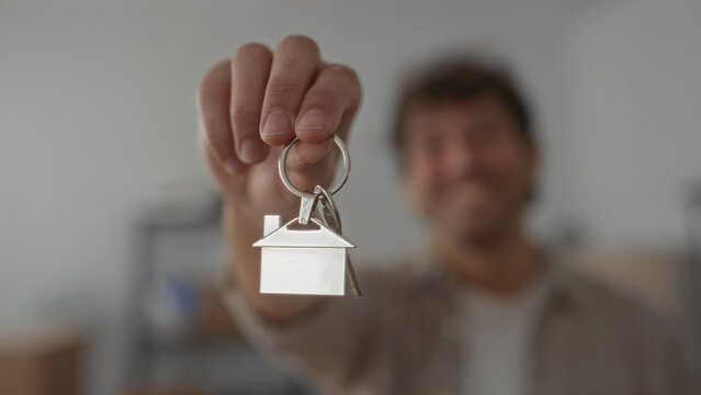 Smiling man holding house keychain, symbolizing new home ownership in a warm indoor setting.