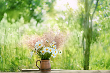 Beautiful summer background. flowers bouquet in clay mug on wooden table in garden. rustic floral composition of chamomile and fluffy grass. summer blossom season. template for design. copy space