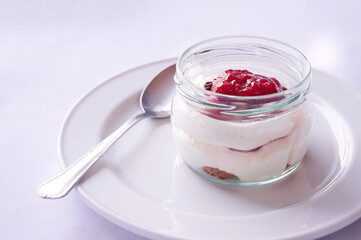 Creamy Greek yogurt mousse with berries and strawberry jam served as a homemade dessert in a glass container at a restaurant. Handmade dessert recipes.
