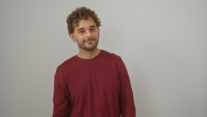 Young hispanic man in a red shirt standing over an isolated white background, showcasing a handsome and attractive adult male with curly hair and casual appearance.
