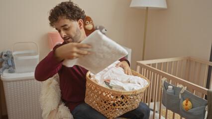 Young man in bedroom arranging baby clothes in a basket near cradle and toys, creating a warm home...